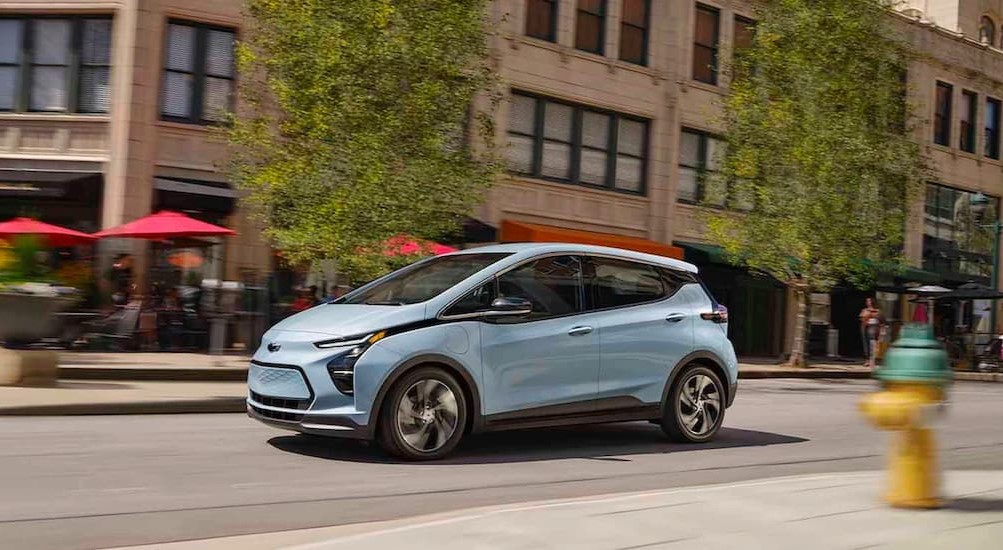 A blue 2022 Chevy Bolt EV is driving to a Chevy dealer near me.