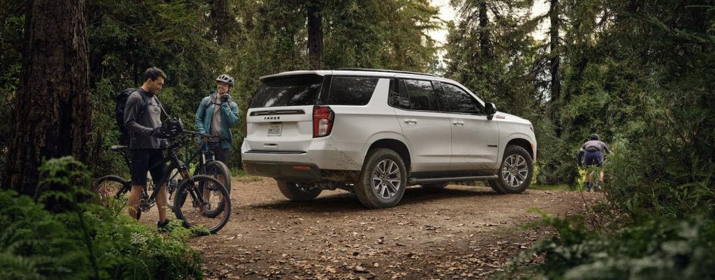 A white 2022 Chevy Tahoe Z71 is shown from the side parked on a trail near two cyclists after leaving a Hondo Chevy dealer.