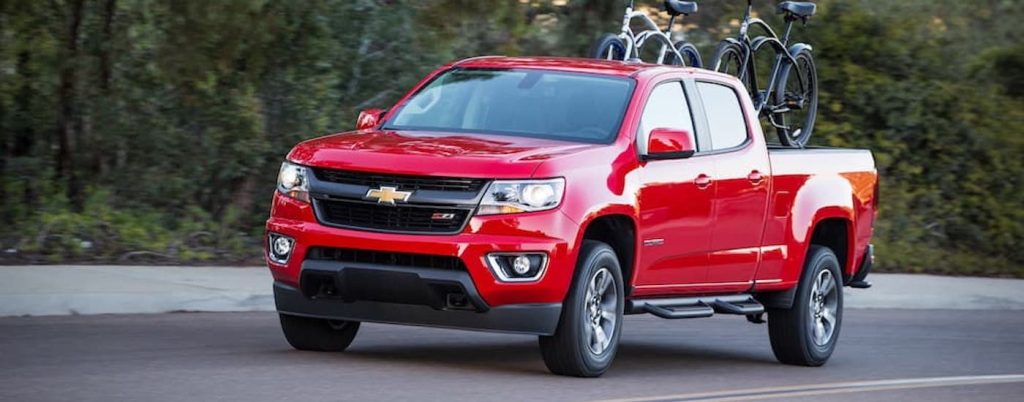 A red Chevy Colorado carrying bicycles on a country road.