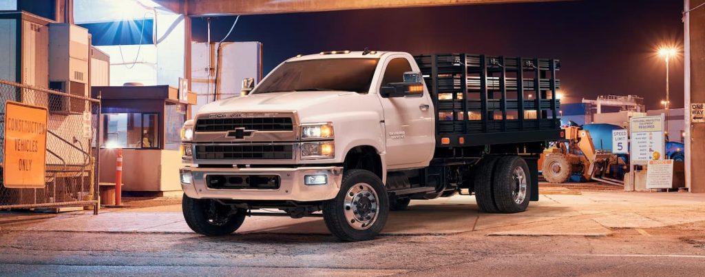 A white 2022 Chevy Silverado 5500HD, a popular work truck for sale, is shown parked at a manufacturing site.