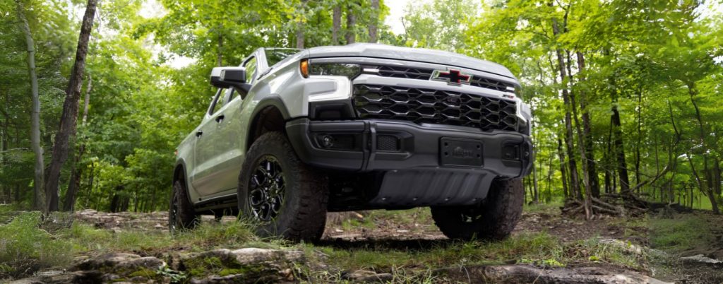 Front view of a white Chevy Silverado 1500 driving in a forest.