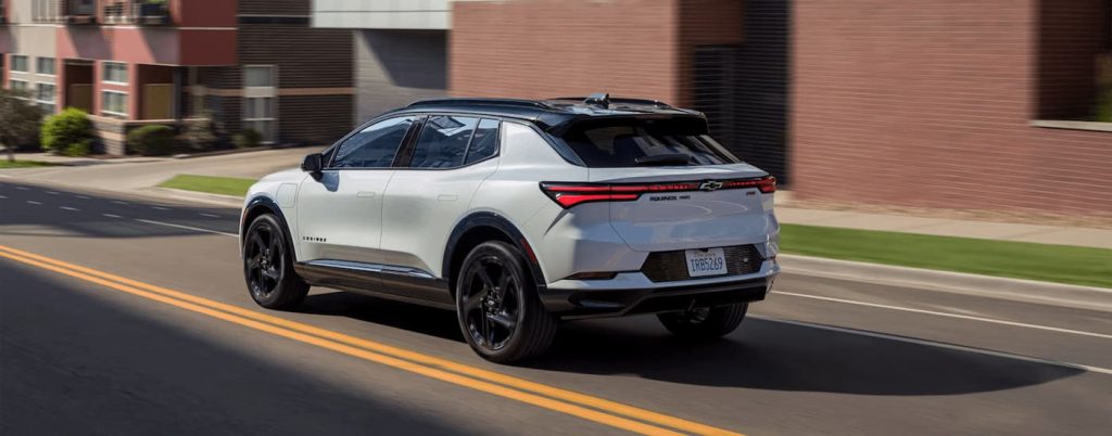 A white Chevy Equinox EV driving on a city road.