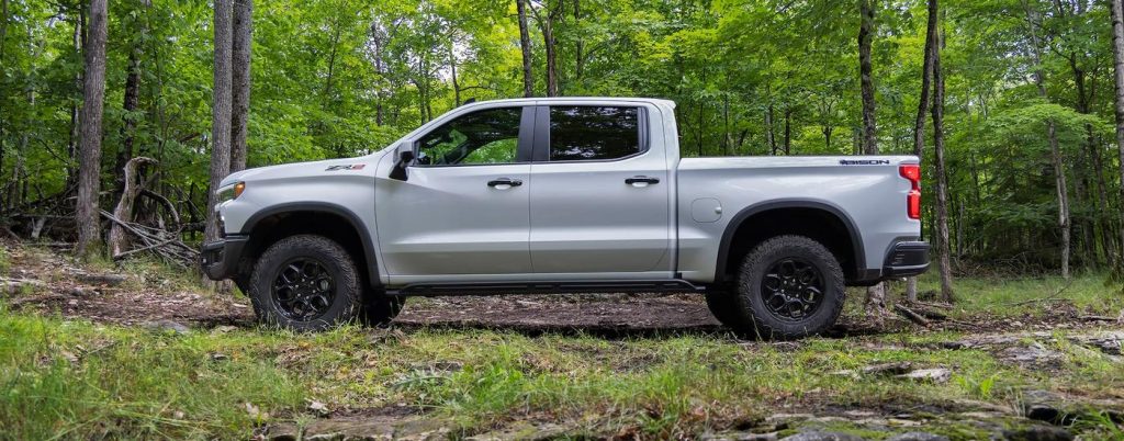 A silver Chevy Silverado parked in a forest.