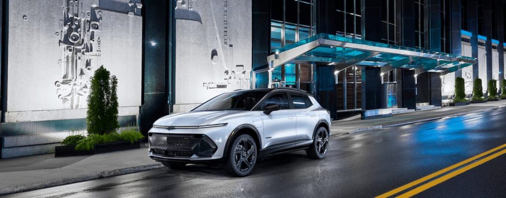 A 2024 white Chevy Equinox EV driving down a city street.