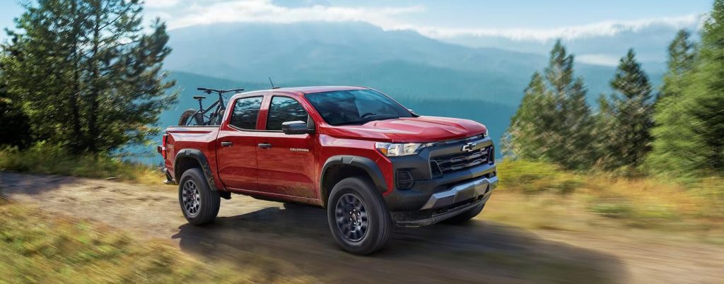 A red Chevy Colorado driving through a forest.