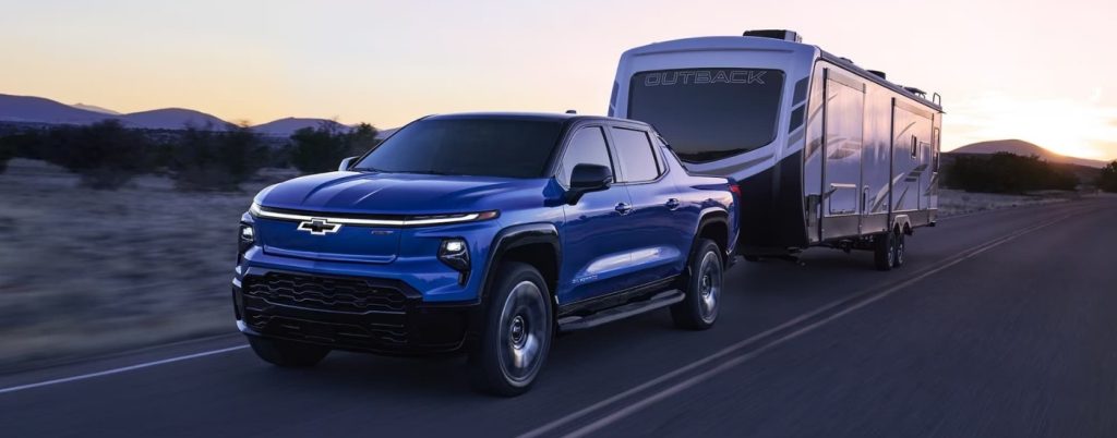 Blue Silverado EV towing a RV on a road.