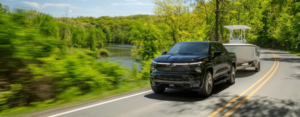 Black Silverado EV towing a boat in the countryside.