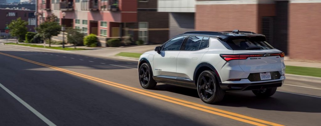 A white Chevy Equinox EV driving down a city road.