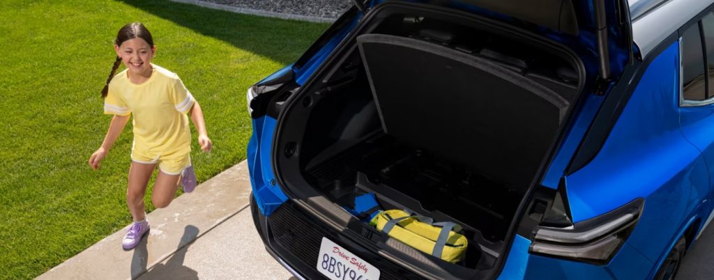 Girl running back open trunk of a blue 2025 Chevy Equinox.
