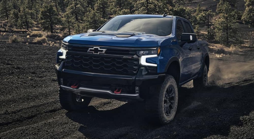 A blue 2022 Chevy Silverado 1500 ZR2 is shown from the front off-roading on a dirt hill after leaving a Bigfoot Chevy dealership.