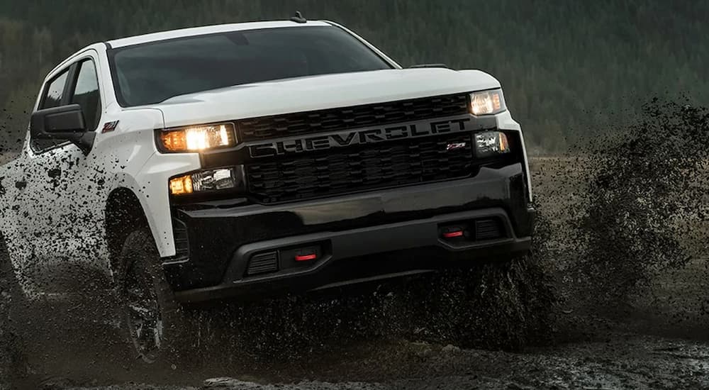 A white 2022 Chevy Silverado 1500 Trail Boss Z71 is shown splashing through mud after visiting a Helotes Chevy dealer.