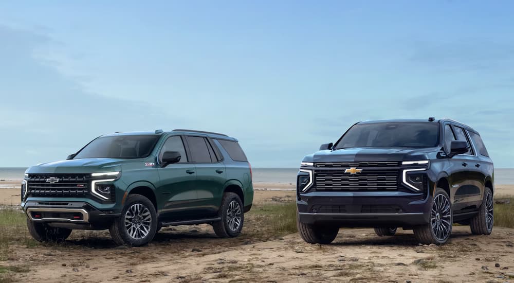 A green 2025 Chevy Suburban Z71 and a black 2025 Chevy Suburban High Country parked off-road