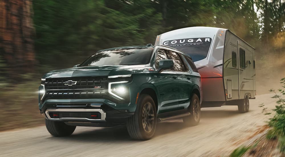 A blue 2026 Chevy Tahoe towing a camper off-road