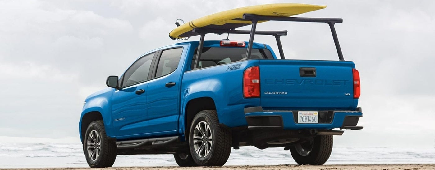 A blue 2022 Chevy Colorado parked on a beach with a surf board attached to the rack.