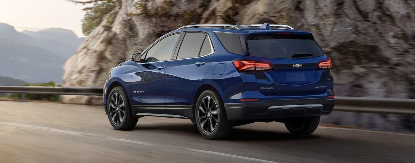 A blue 2022 Chevy Equinox is shown from the rear driving on an open road during a 2022 Chevy Equinox vs 2022 Ford Escape comparison.