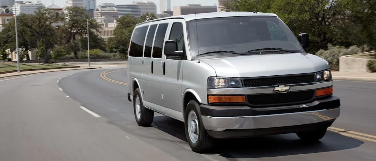 A silver 2022 Chevy Express Van is shown from the front driving on an open road.