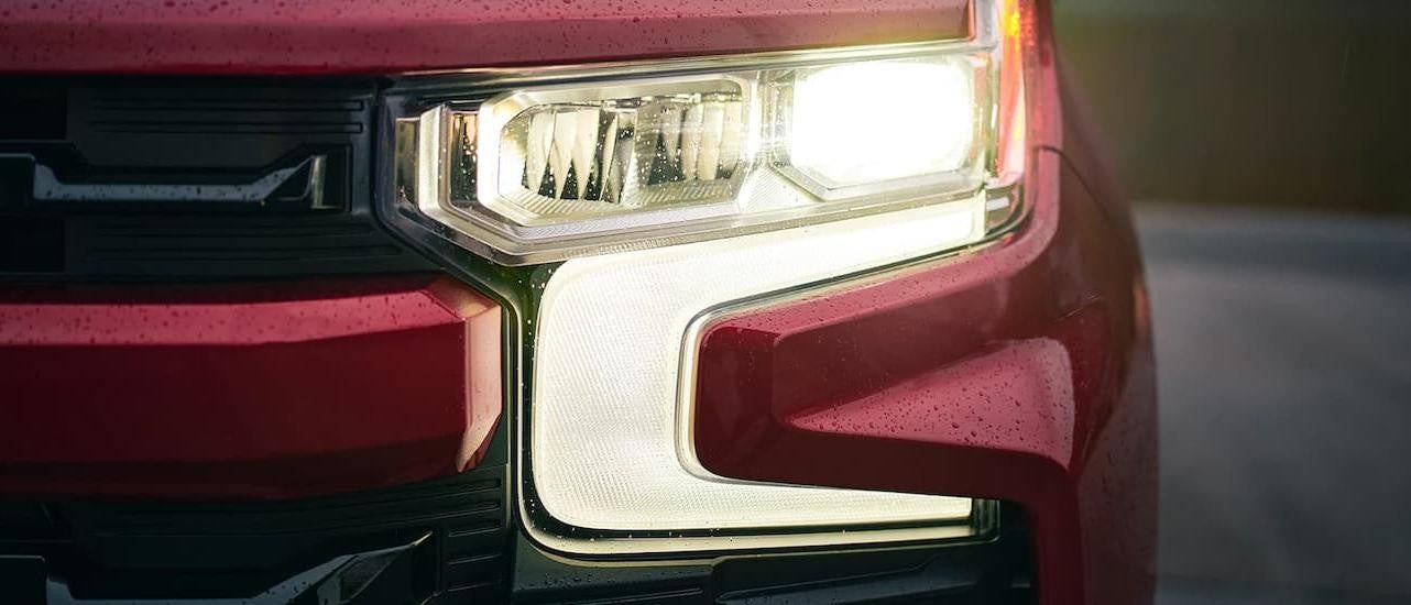 A close up shows the driver side headlight on a red 2022 Chevy Silverado 1500.