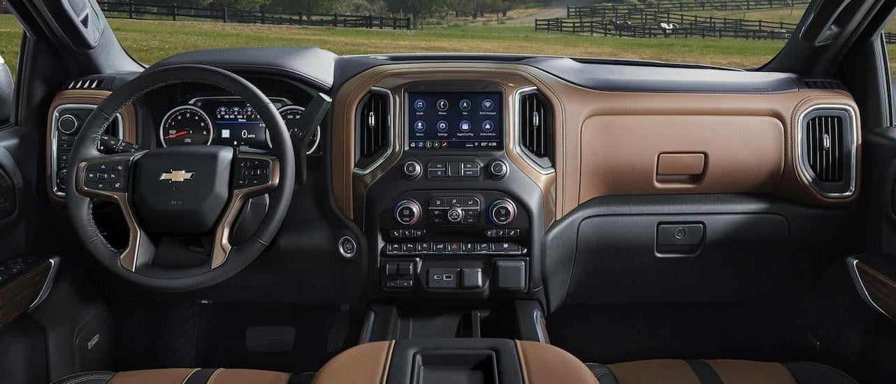 The black and brown interior of a 2022 Chevy Silverado 1500 shows the steering wheel and infotainment screen.