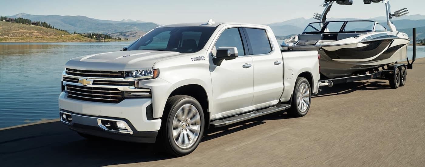 A white 2022 Chevy Silverado 1500 High Country is shown while towing a boat.