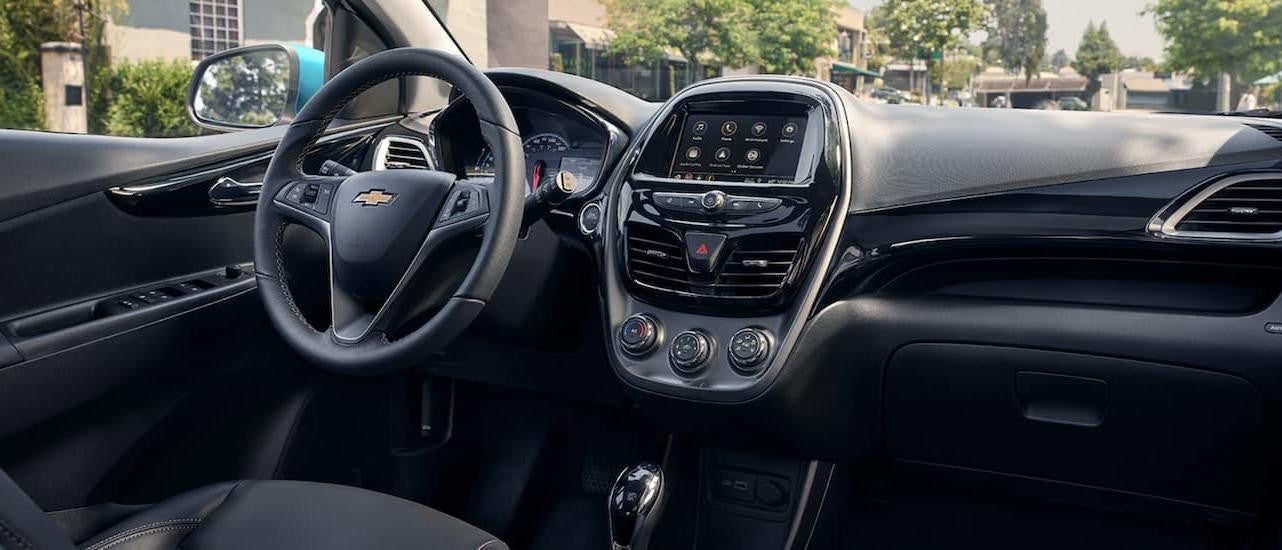 The black interior of a 2022 Chevy Spark shows the steering wheel and infotainment screen.