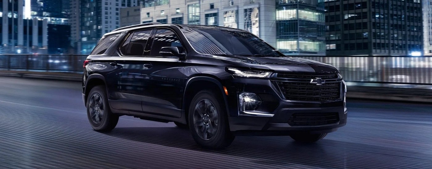 A black 2022 Chevy Traverse Midnight Editiong driving on a city street at night.