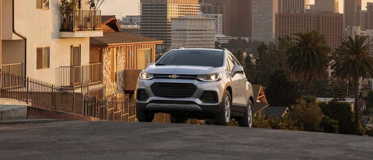 A silver 2022 Chevy Trax is shown from the front driving on an open road through a city.