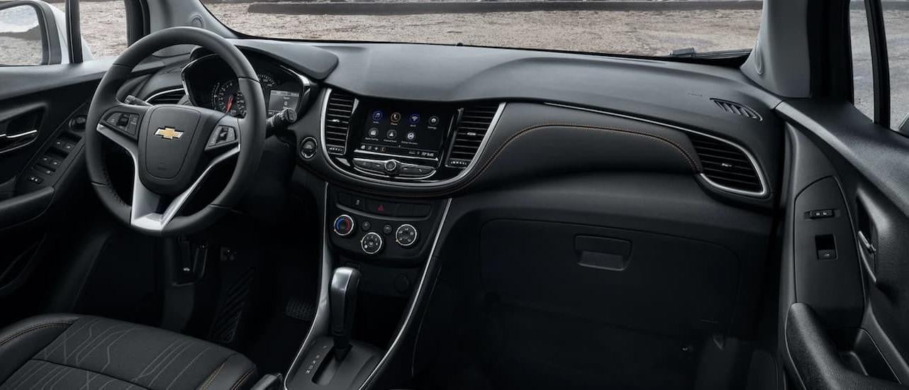 The black interior of a 2022 Chevy Trax shows the steering wheel and infotainment screen.