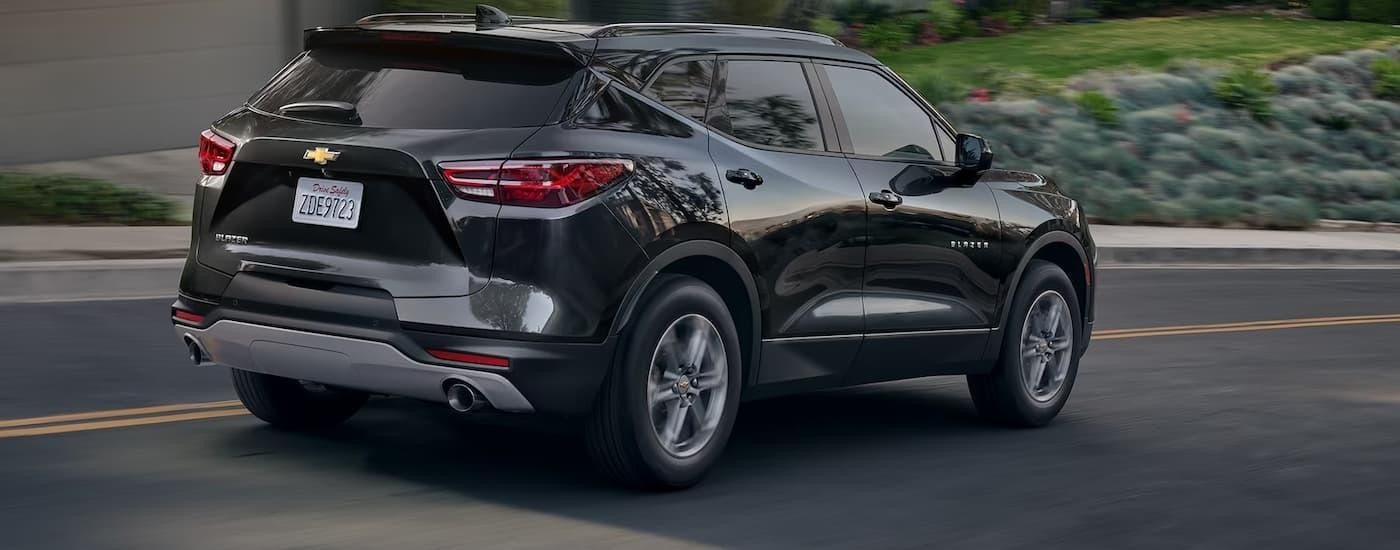 A black 2024 Chevy Blazer is shown from a rear angle driving on an open road.