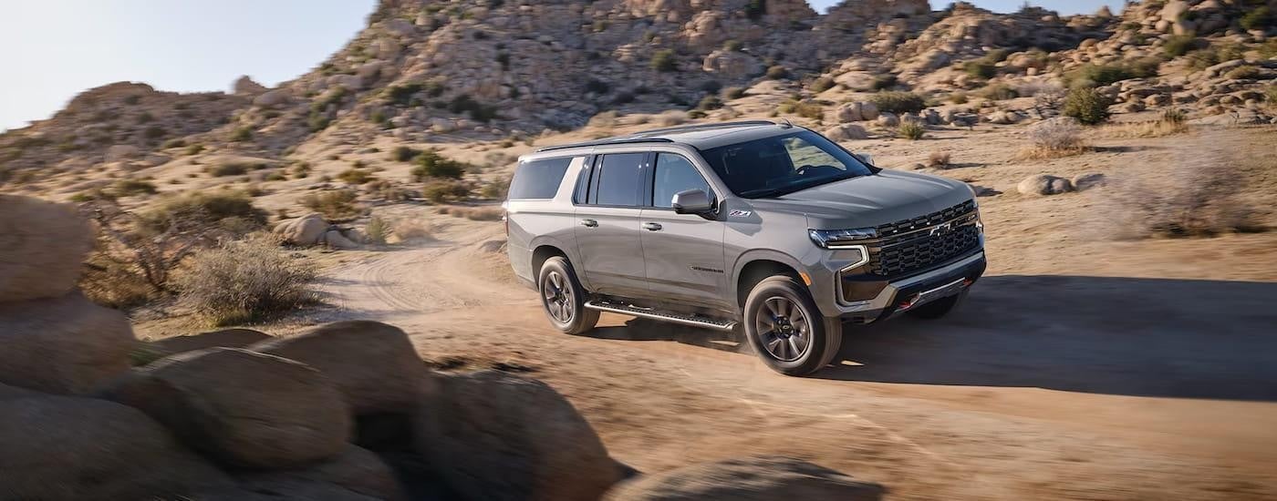 A grey 2024 Chevy Suburban Z71 is shown driving on a dusty desert area.