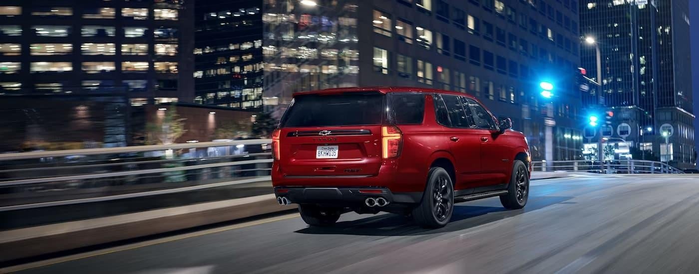 A red 2024 Chevy Tahoe RST is shown from the rear driving on a highway towards a city.