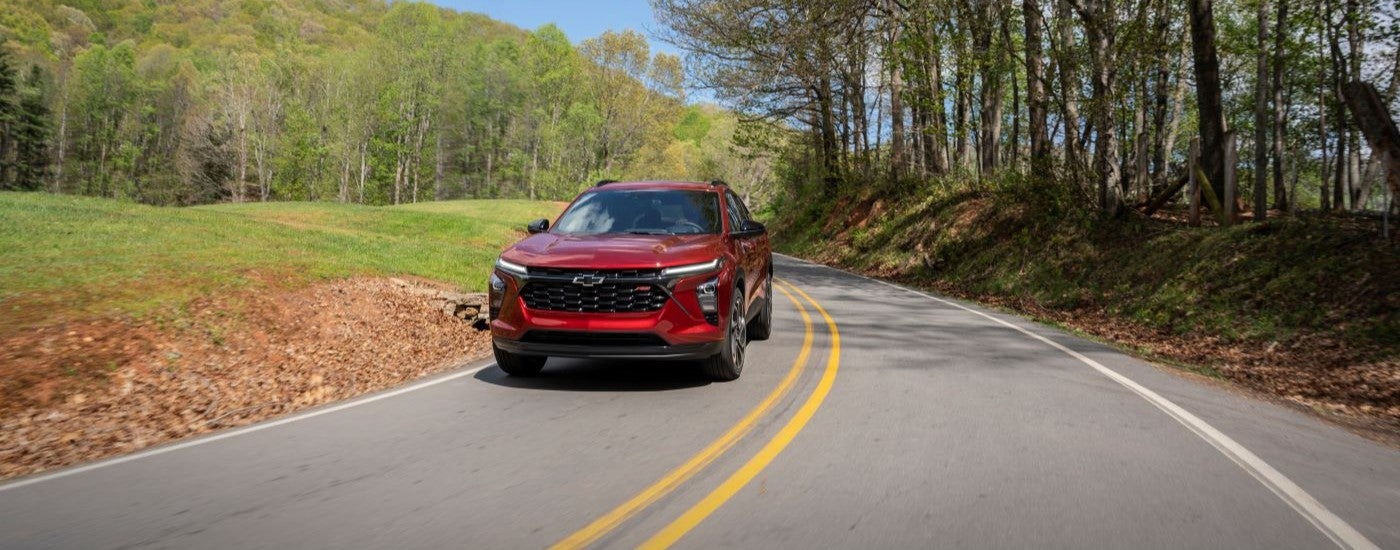 A red 2024 Chevy Trax RS driving by trees.