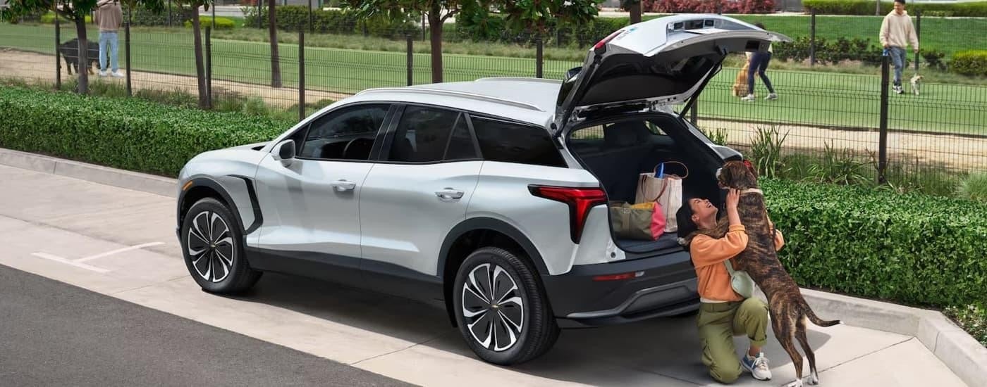 A woman is playing with a dog next to a grey 2025 Chevy Blazer EV.