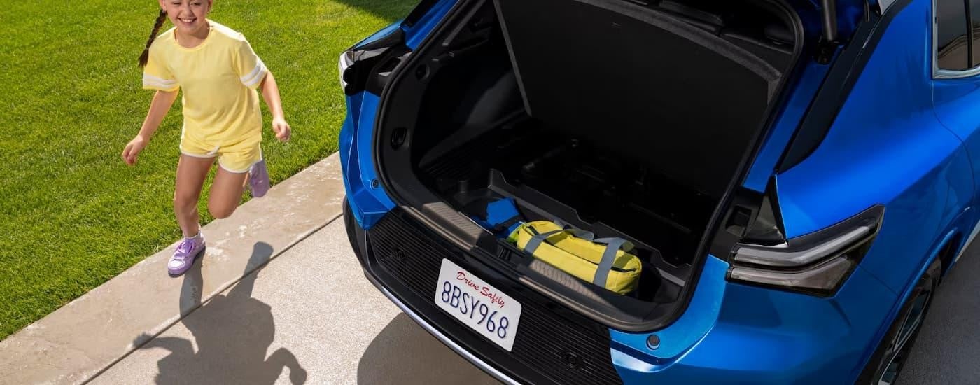 A child is running near the open rear cargo door of a blue 2025 Chevy Equinox EV LT.