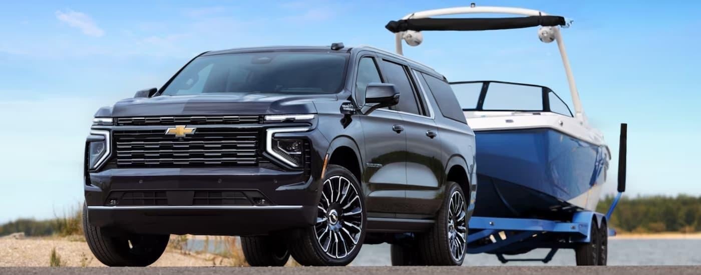 A black 2025 Chevy Suburban is towing a boat out of a lake.