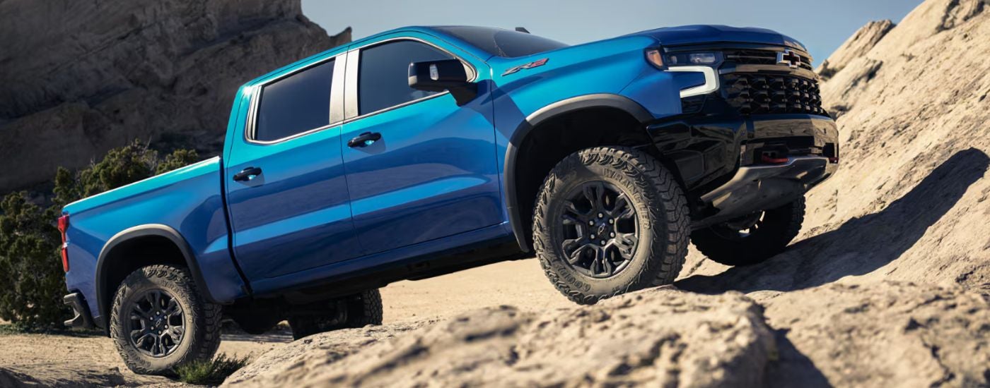 2026 Blue Chevy Silverado driving up rocks.