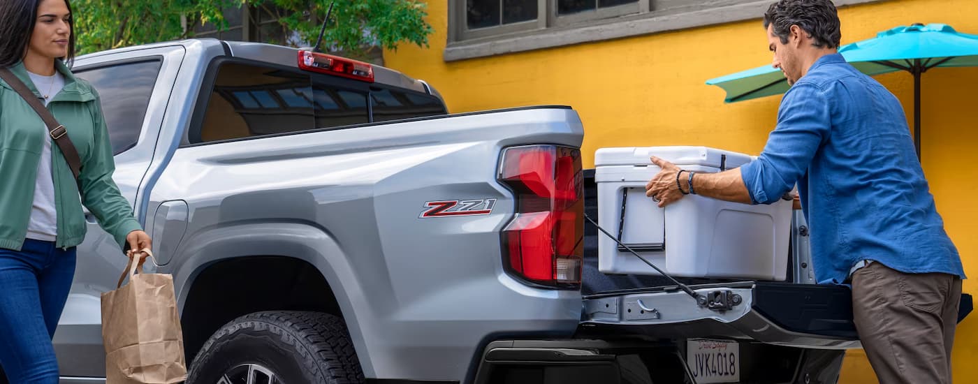 Person putting a cooler in the bed of a grey 2026 Chevy Colorado