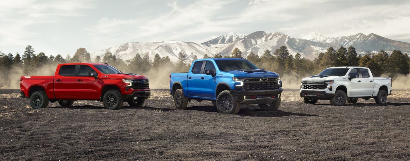 A trio of 2026 Chevy Silverados in red, blue and white parked in front of a mountain.