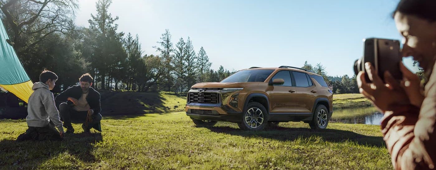A brown 2027 Chevy Equinox Activ parked near a family taking photos.