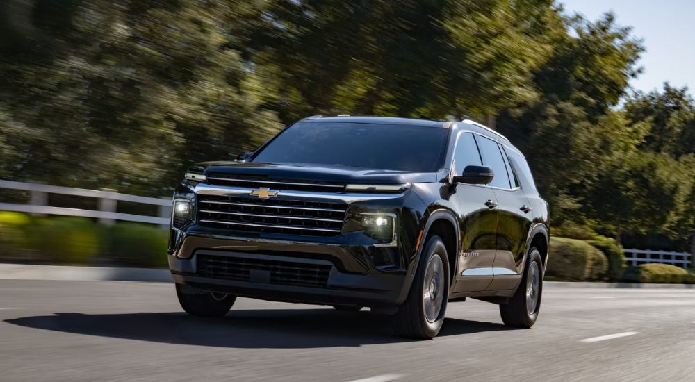 A black 2027 Chevy Traverse driving by a fence.