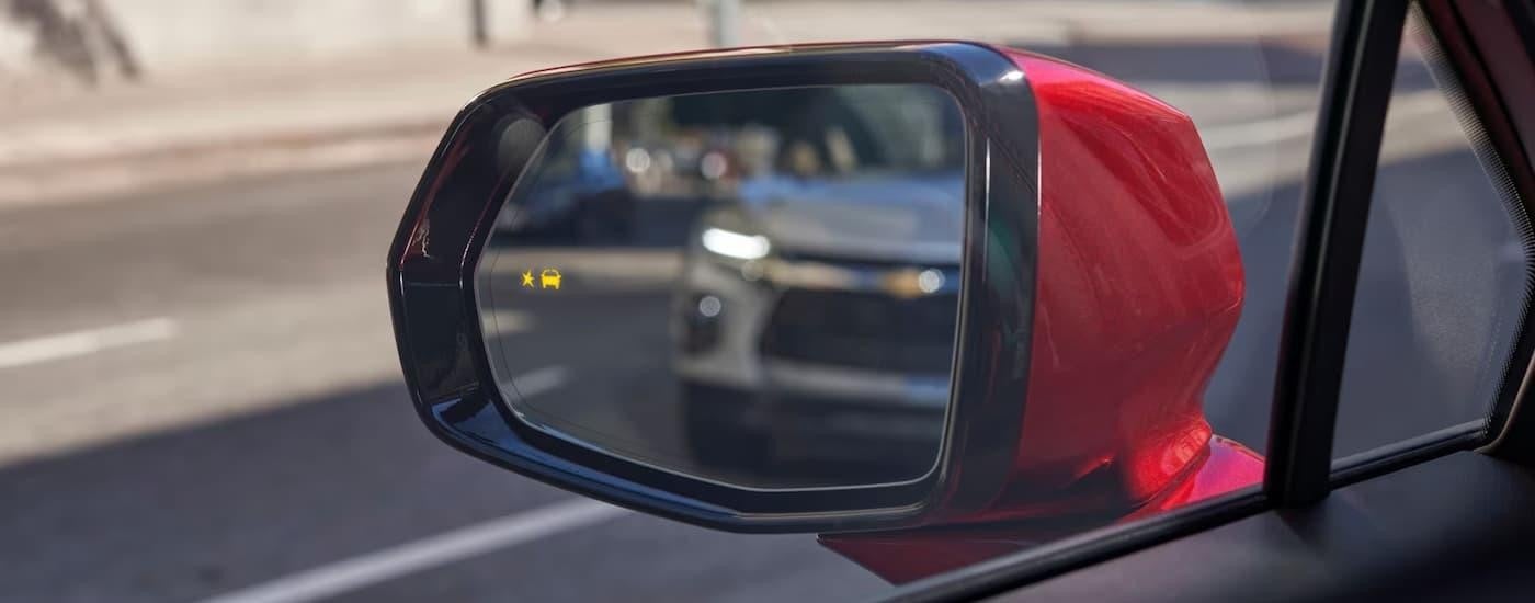 A silver 2023 Chevy Blazer is shown in the side mirror of a red vehicle.