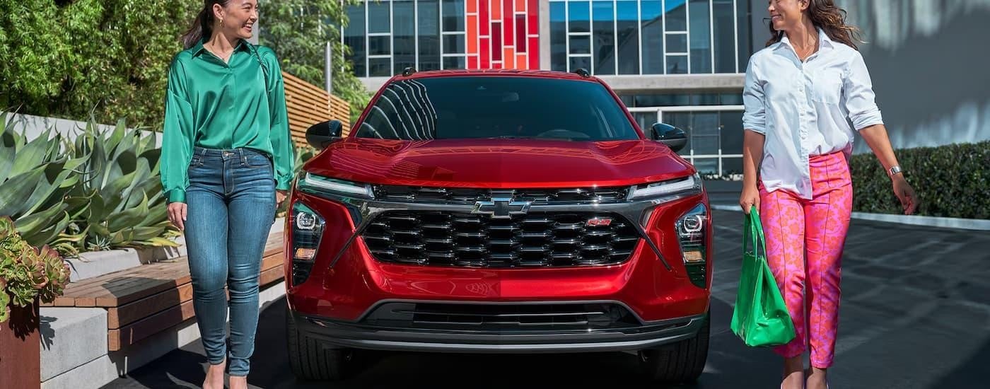 Two people are walking away from a red 2025 Chevy Equinox RS parked in a city.