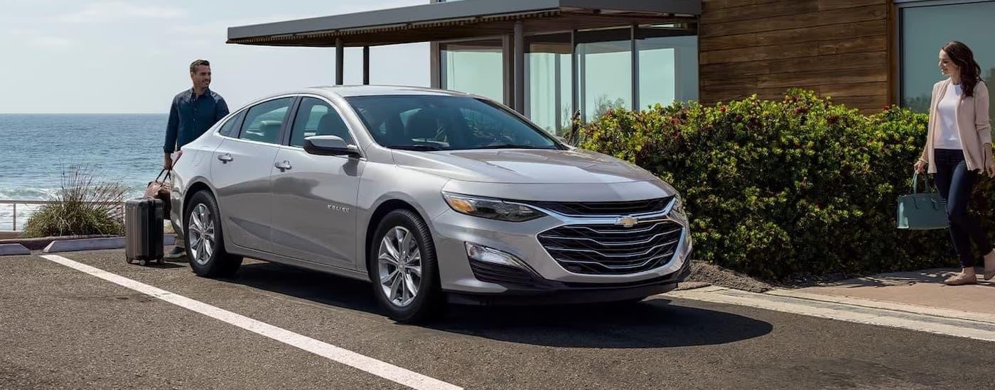 A silver 2024 Chevy Malibu is parked near a hotel by the ocean.