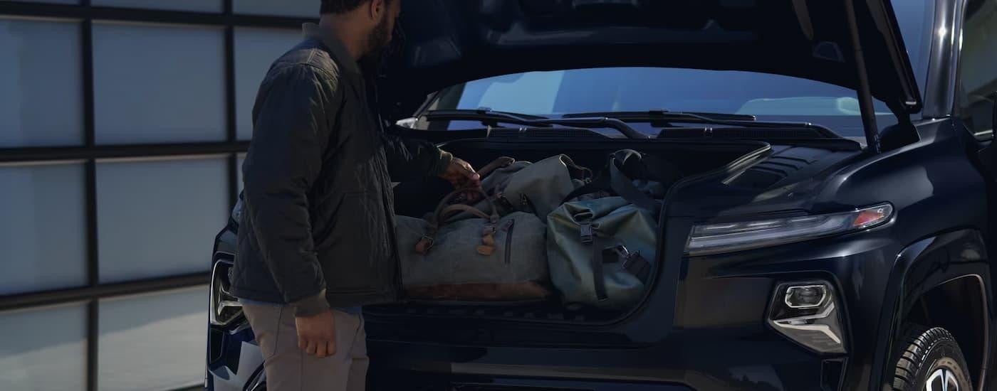 A man is getting luggage out of the frunk of a black 2025 Chevy Silverado EV.