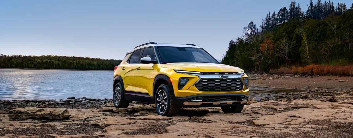 A yellow 2024 Chevy Trailblazer is shown parked on rocks near a body of water.
