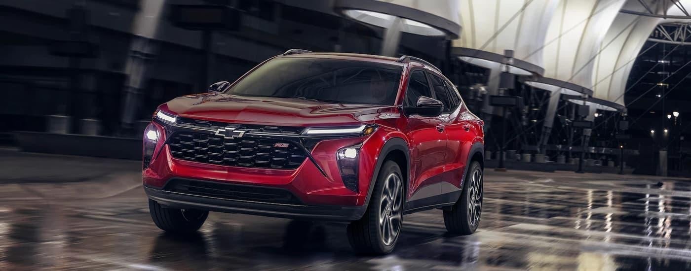 A red 2024 Chevy Trax RS is driving on a city street at night.