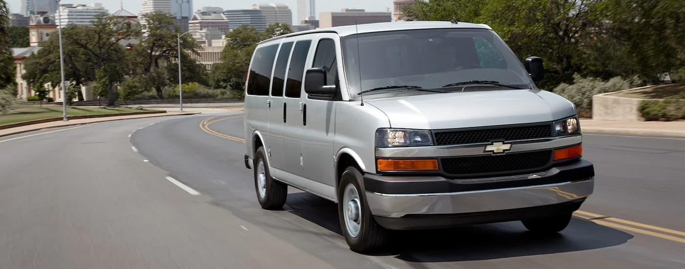 A silver 2022 Chevy Express Van driving on a city street after viewing Chevy fleet vehicles for sale.