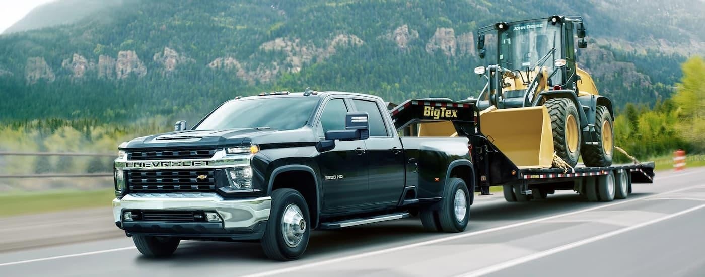 A black 2022 Chevy Silverado 3500HD WT towing heavy machinery on a highway.