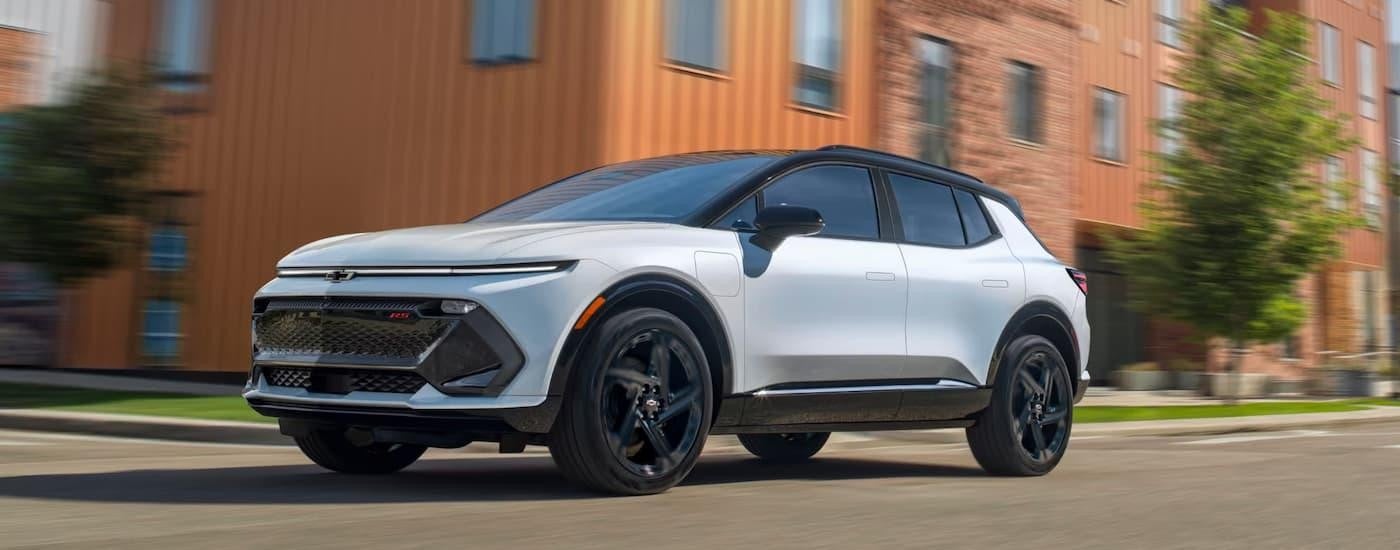 A white 2025 Chevy Equinox EV RS, a popular electric vehicle for sale, is driving on a city street.