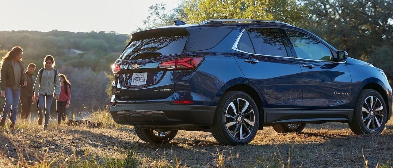 A family is shown hiking near a dark blue 2022 Chevy Equinox Premier.