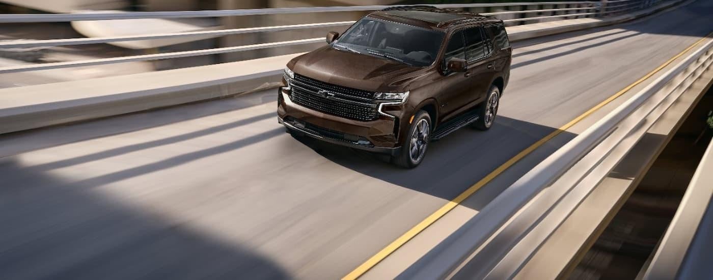 A brown 2023 Chevy Tahoe is shown driving on a city highway after leaving a San Antonio Chevy dealer.